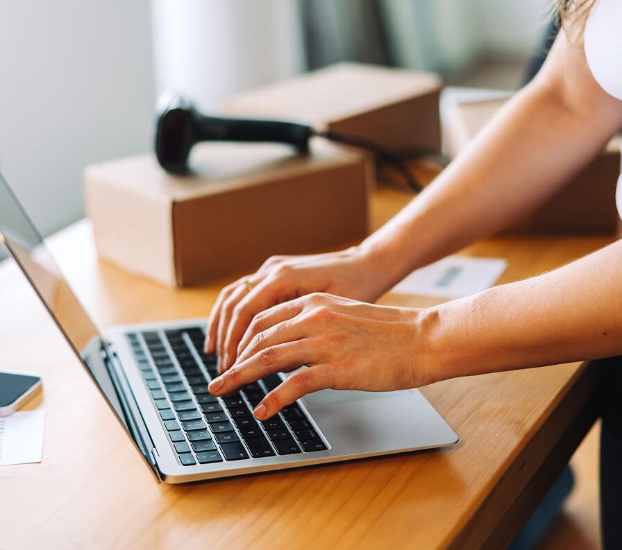 Typing on a laptop in front of packed parcels and a barcode scanner