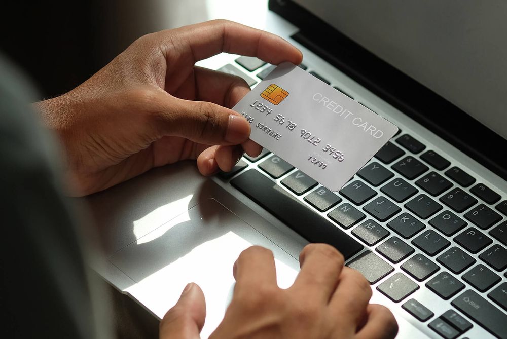 A shopper's hands holding a bank card above a laptop keyboard, ready to pay online.