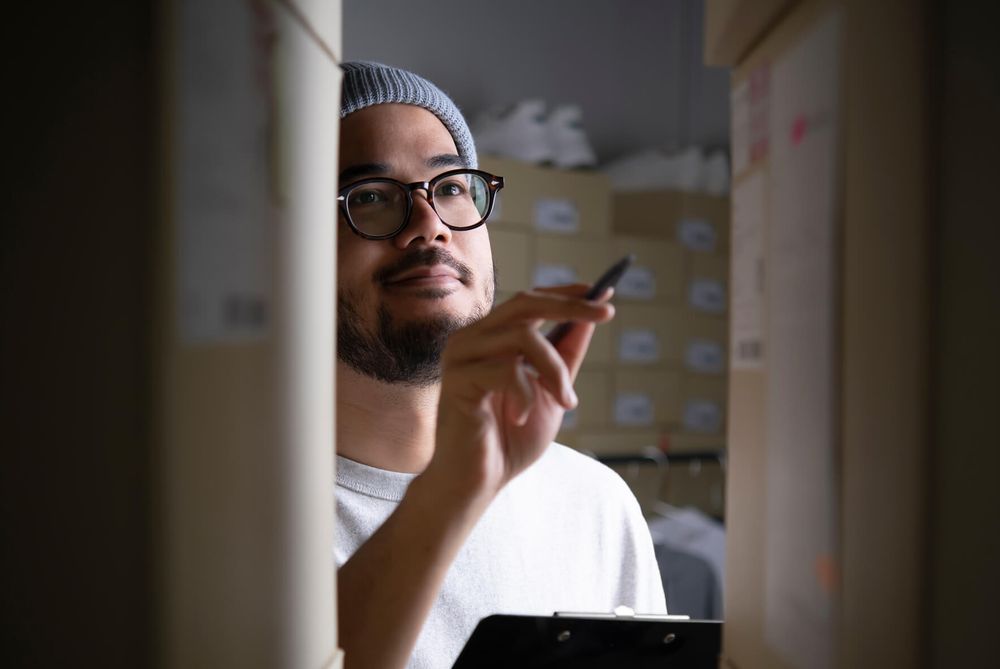 Person with a clipboard checking labelled shipping boxes in a small order preparation room