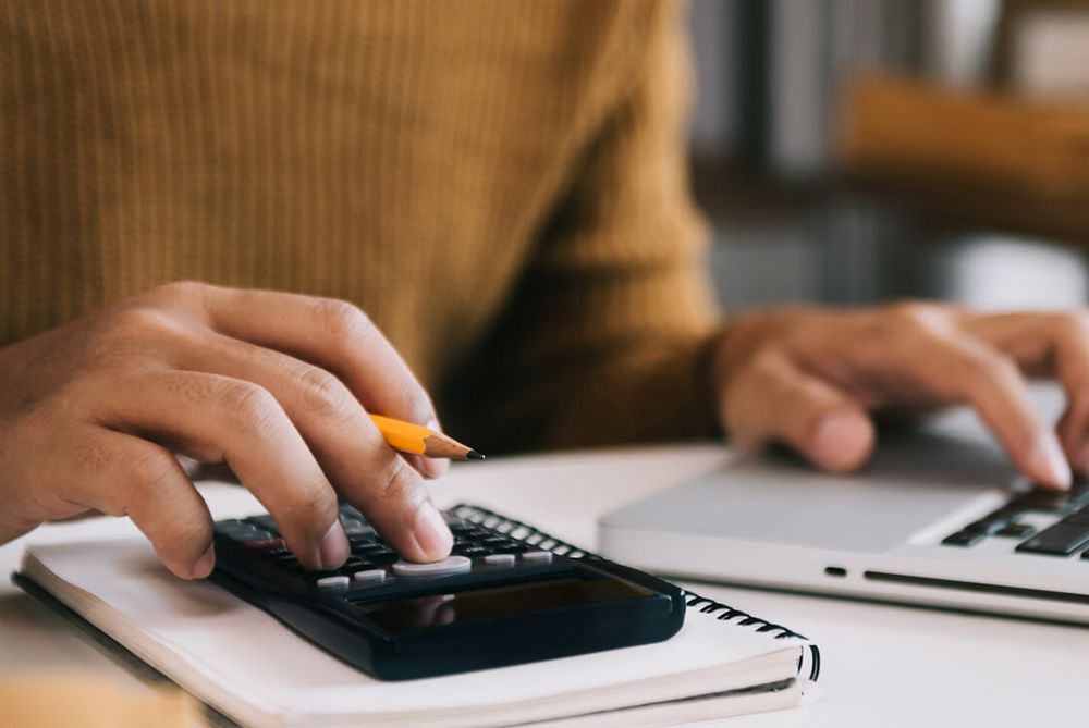 Hands using a calculator resting on a notebook, beside an open laptop