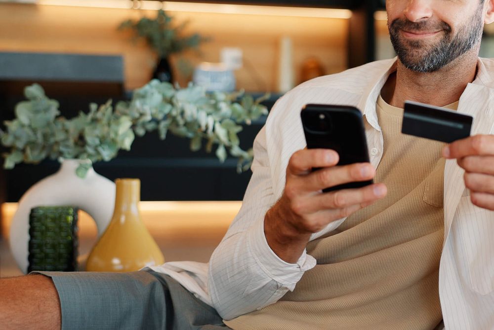Une cliente règle un achat en ligne depuis son téléphone, carte bancaire à la main