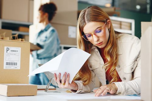 Commerçante lisant des documents dans son espace d'expédition, un colis étiqueté posé devant elle
