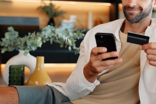 Uma cliente paga uma compra online a partir do telemóvel, com o cartão na mão